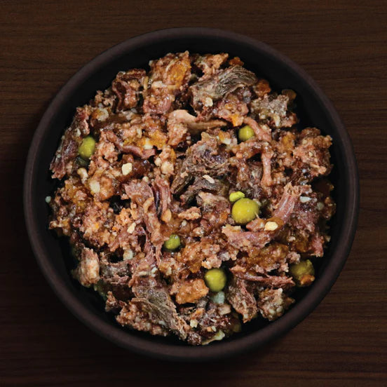 Dog food mix with visible ingredients in a black bowl on a wooden surface