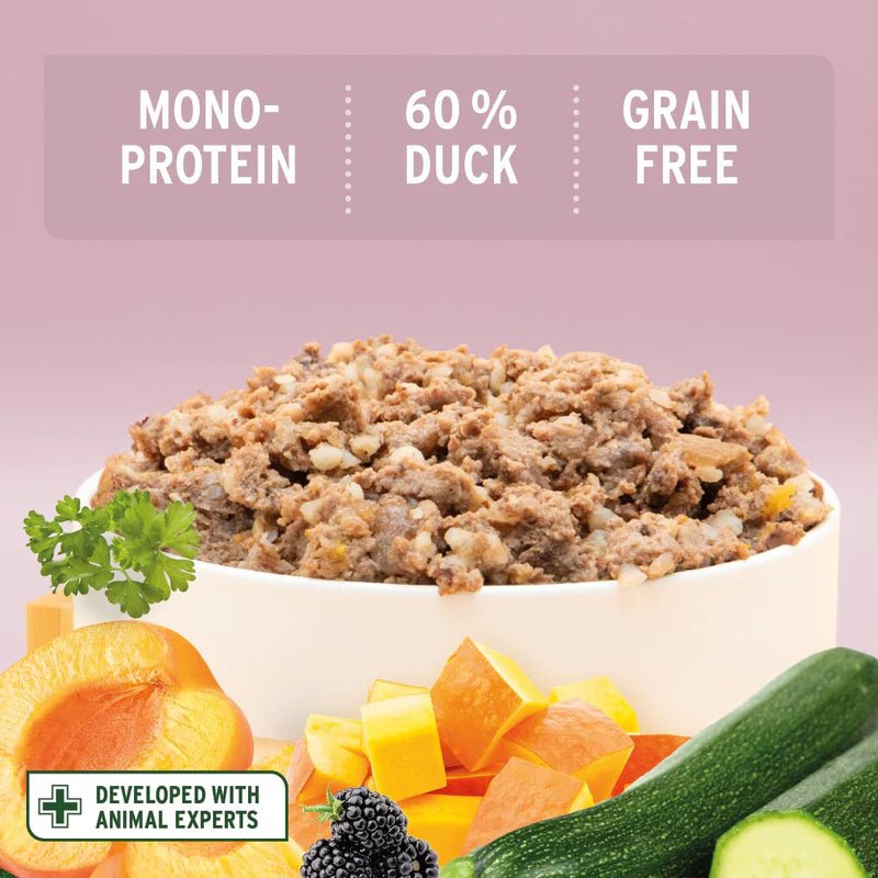 Dish of duck-based pet food with vegetables on a pink background, featuring text about protein type and grain freedom.
